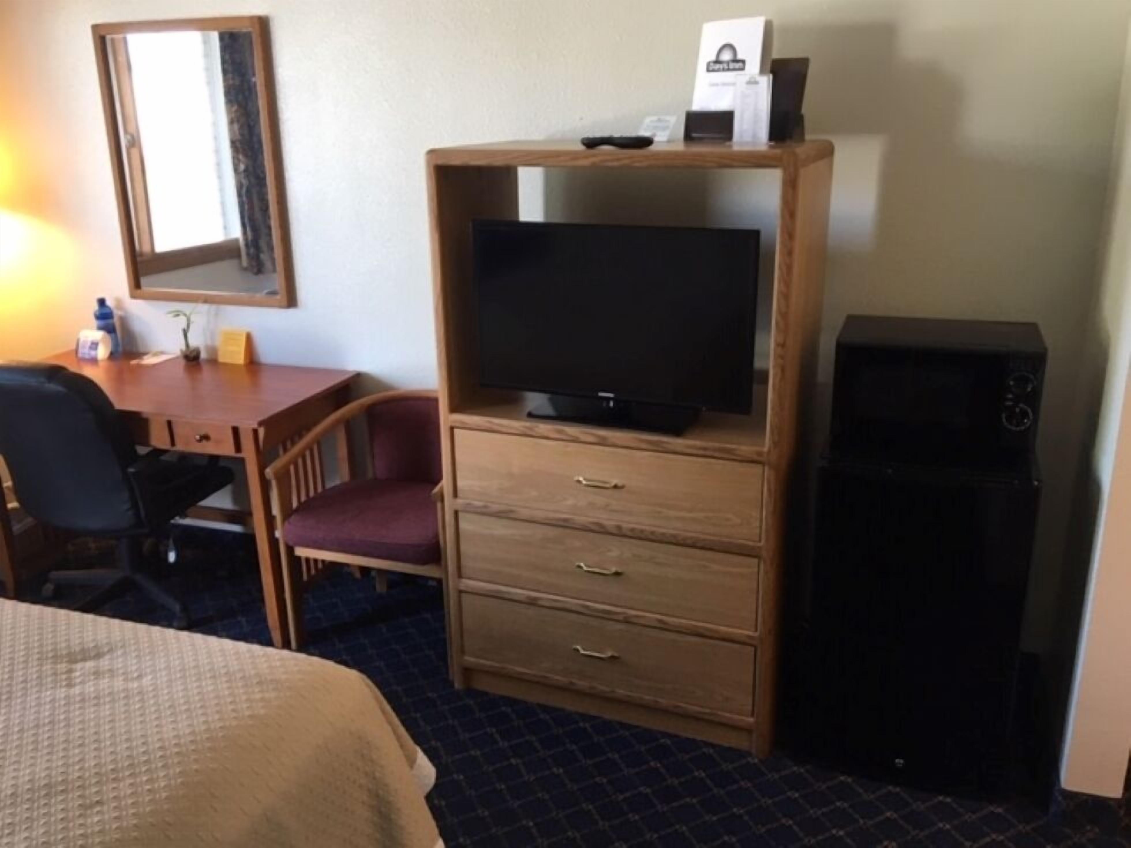 Une chambre d’hôtel comprenant un lit, un bureau avec une chaise, un téléviseur posé sur un meuble en bois et un haut-parleur noir.