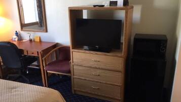 Habitación de hotel con una cama, un escritorio con silla, un televisor sobre un mueble de madera y un altavoz negro.