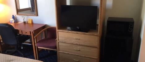 Une chambre d’hôtel comprenant un lit, un bureau avec une chaise, un téléviseur posé sur un meuble en bois et un haut-parleur noir.