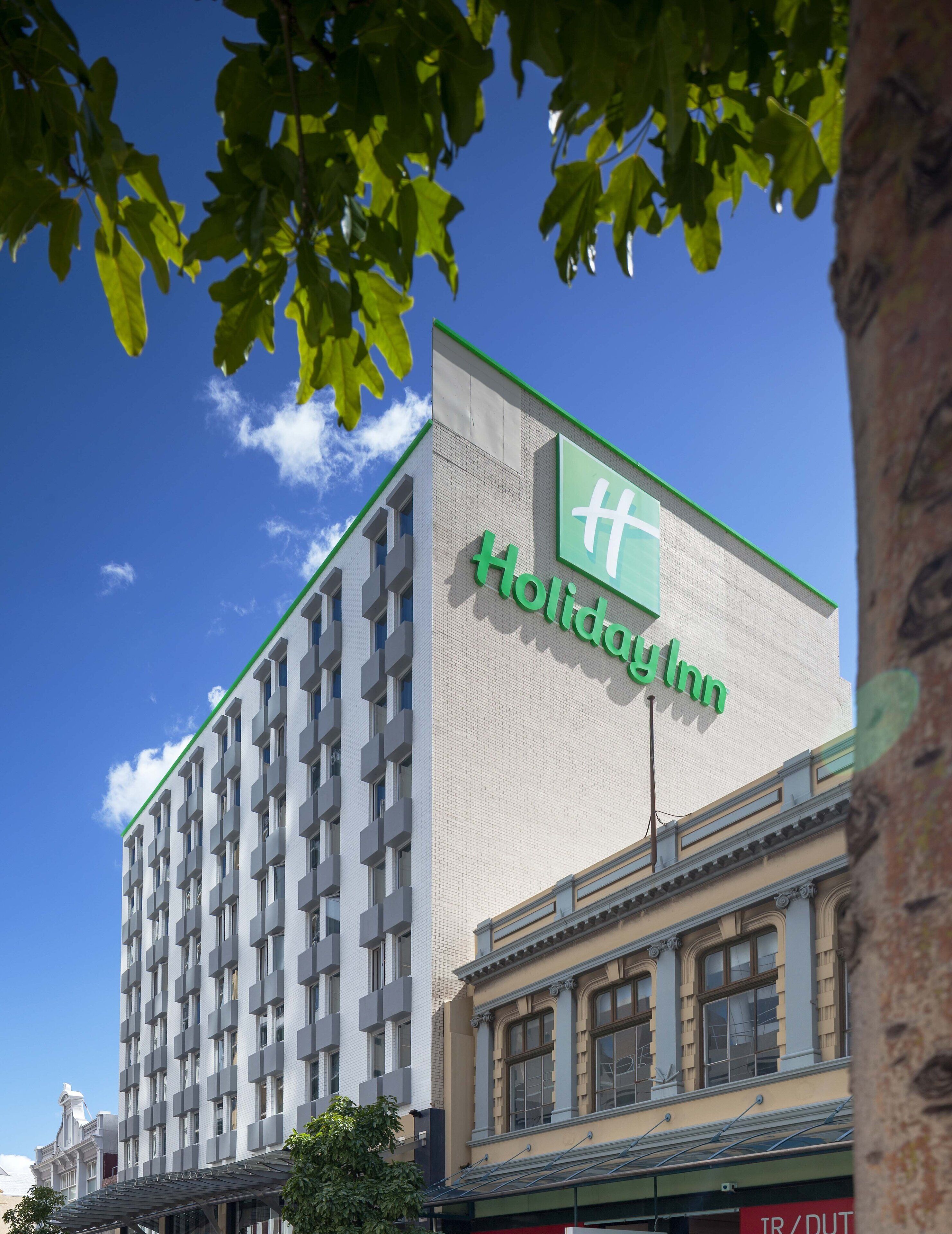 Un hôtel Holiday Inn doté d’une façade moderne, de grandes fenêtres et d’un logo vert bien visible.