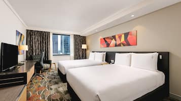 A hotel room with two beds, a desk with a TV, and a large window with curtains.