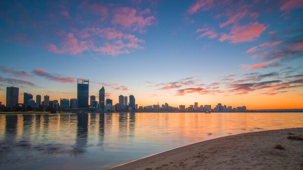 A city skyline at sunset with buildings reflected in calm water. - Holiday Inn Perth City Centre by IHG (Perth)