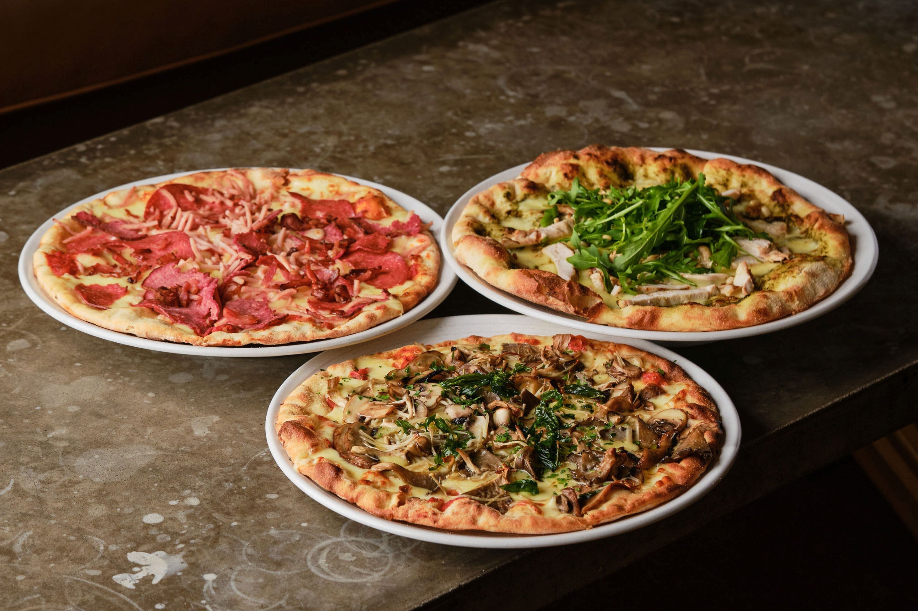 Three pizzas on white plates on a table.
