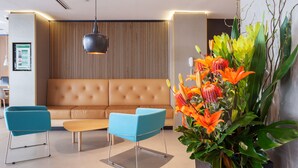 A modern lobby with a sofa, two blue chairs, a wooden panel wall, and a large floral arrangement. - Holiday Inn Perth City Centre by IHG (Perth)
