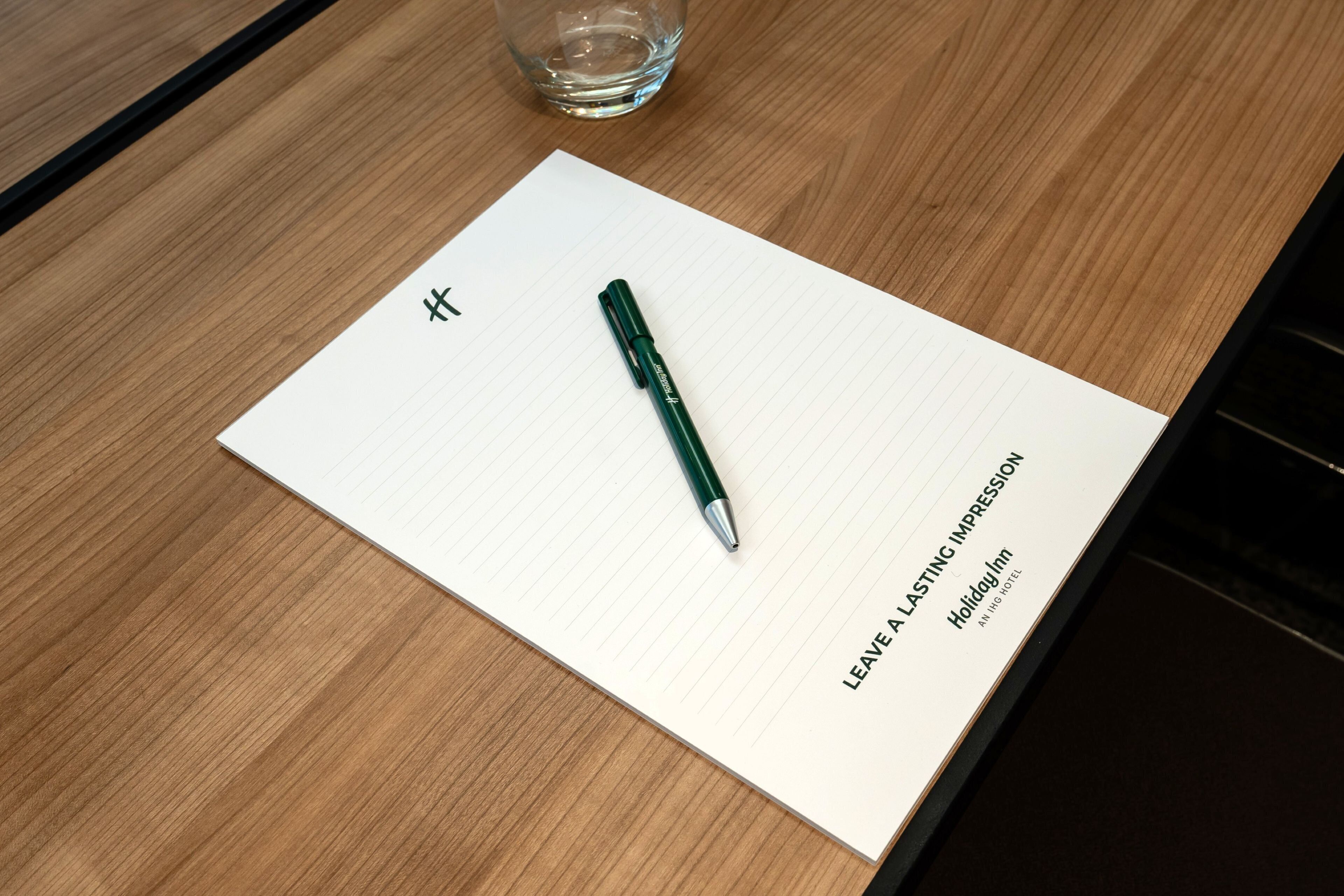 Un carnet avec un stylo posé sur une table en bois. On peut lire sur le carnet les mots suivants : « LAISSEZ UNE IMPRESSION INDÉLEBILE » et « Holiday Inn ».