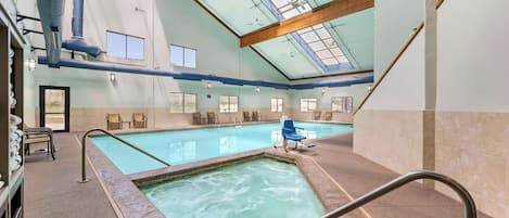 An indoor swimming pool with clear glass ceilings, multiple windows, and a seating area with chairs.