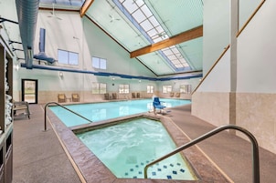 Una piscina interior con techos de vidrio transparente, varias ventanas y una zona de estar con sillas.