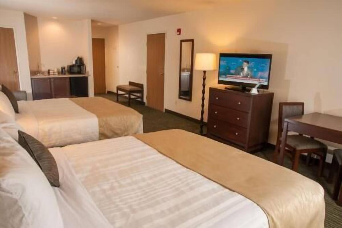 A hotel room with two beds, a TV, a desk, a chair, a dresser, and a mirror.