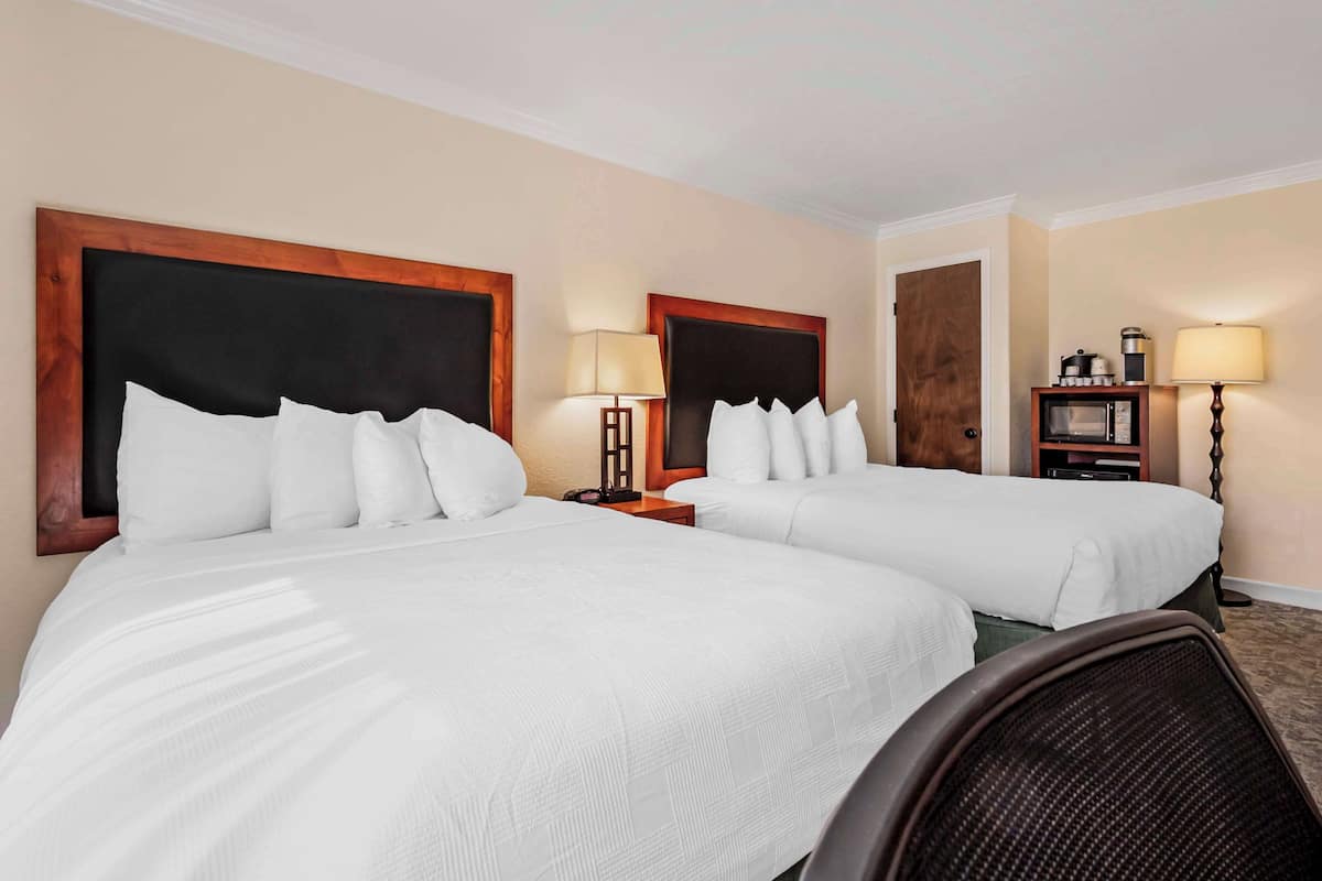 A hotel room with two beds, a nightstand with a lamp, a microwave, and a coffee maker.