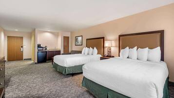 A hotel room with two beds, a desk, a chair, a lamp, and a small kitchenette.