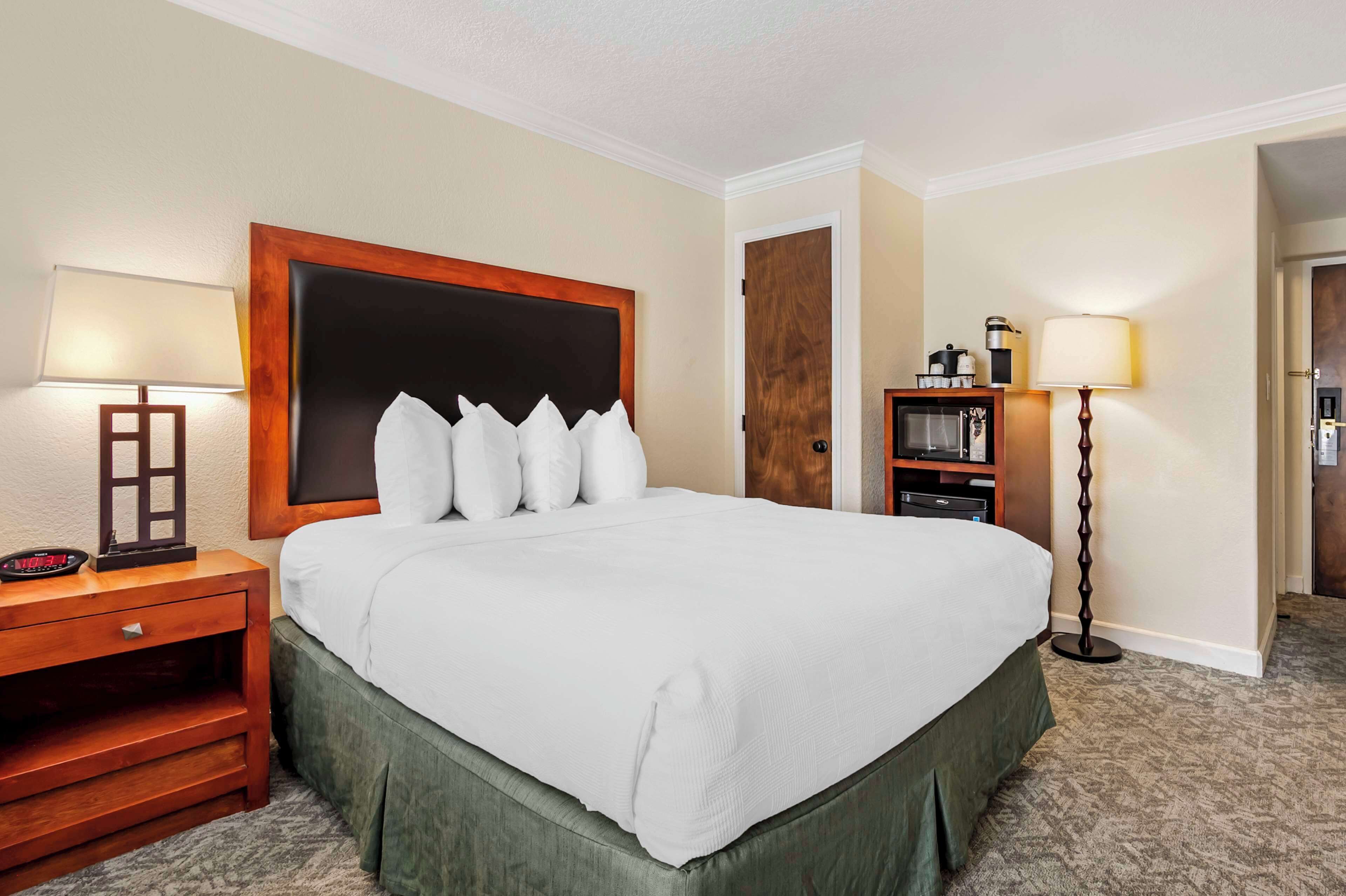 A hotel room with a large bed, two bedside tables, a nightstand, a lamp, a dresser, and a door.