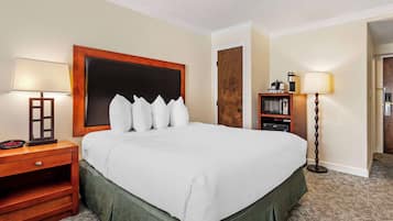 Een hotelkamer met een groot bed, twee nachtkastjes, een kastje, een lamp, een kapstok en een deur.