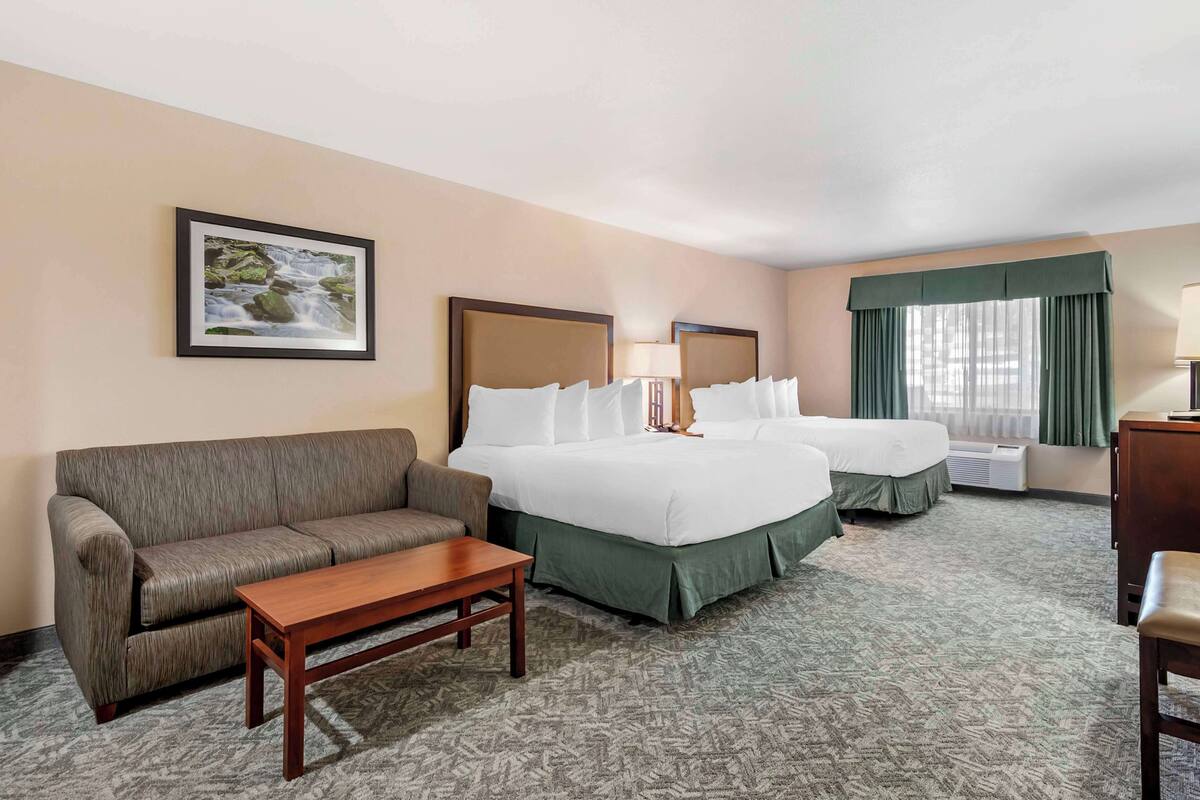 A hotel room with two beds, a sofa, a small table, and a framed picture on the wall.