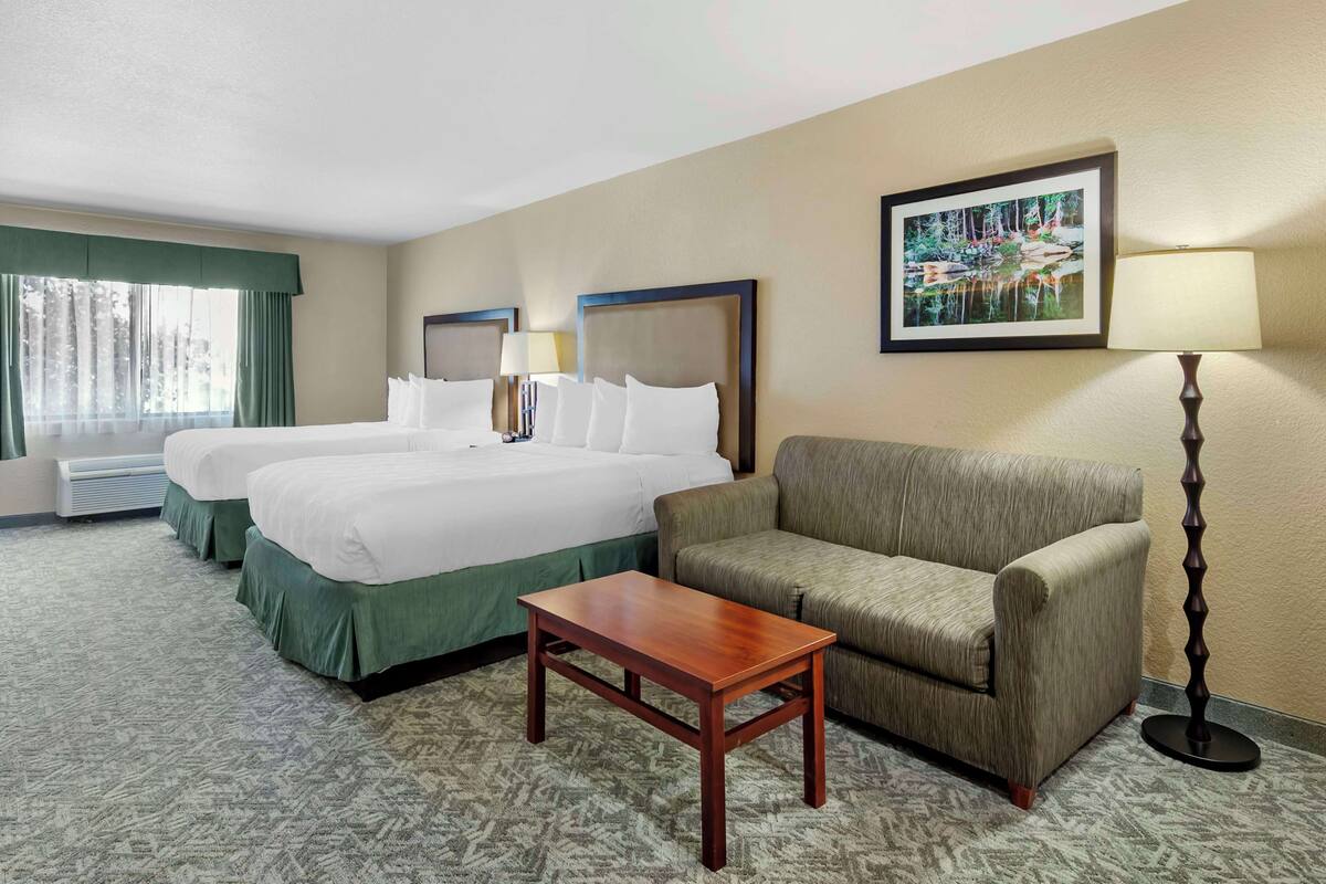 A hotel room with two beds, a sofa, a table, a lamp, and a painting on the wall.