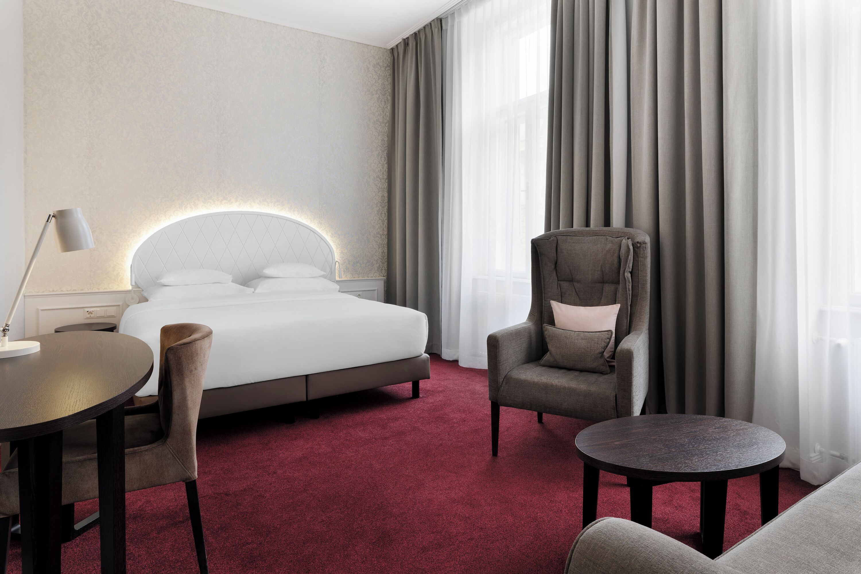 A hotel room with a bed, a chair, a round table, and a lamp.