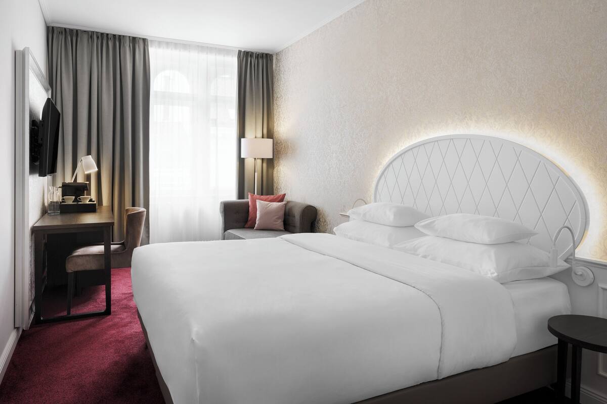 Een hotelkamer met een groot bed, een bureau, een stoel, een televisie en een lamp.