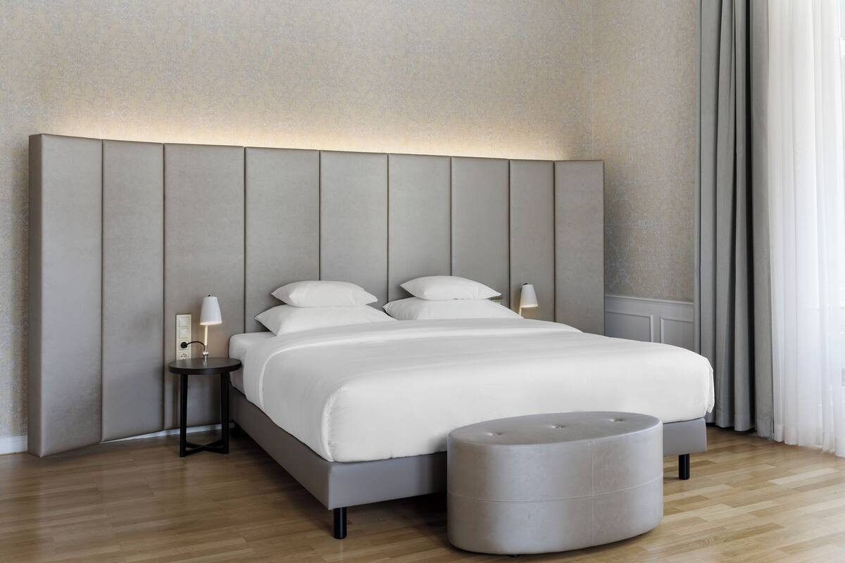 Een moderne slaapkamer met een groot bed, een nachtkastje en een rond poef.