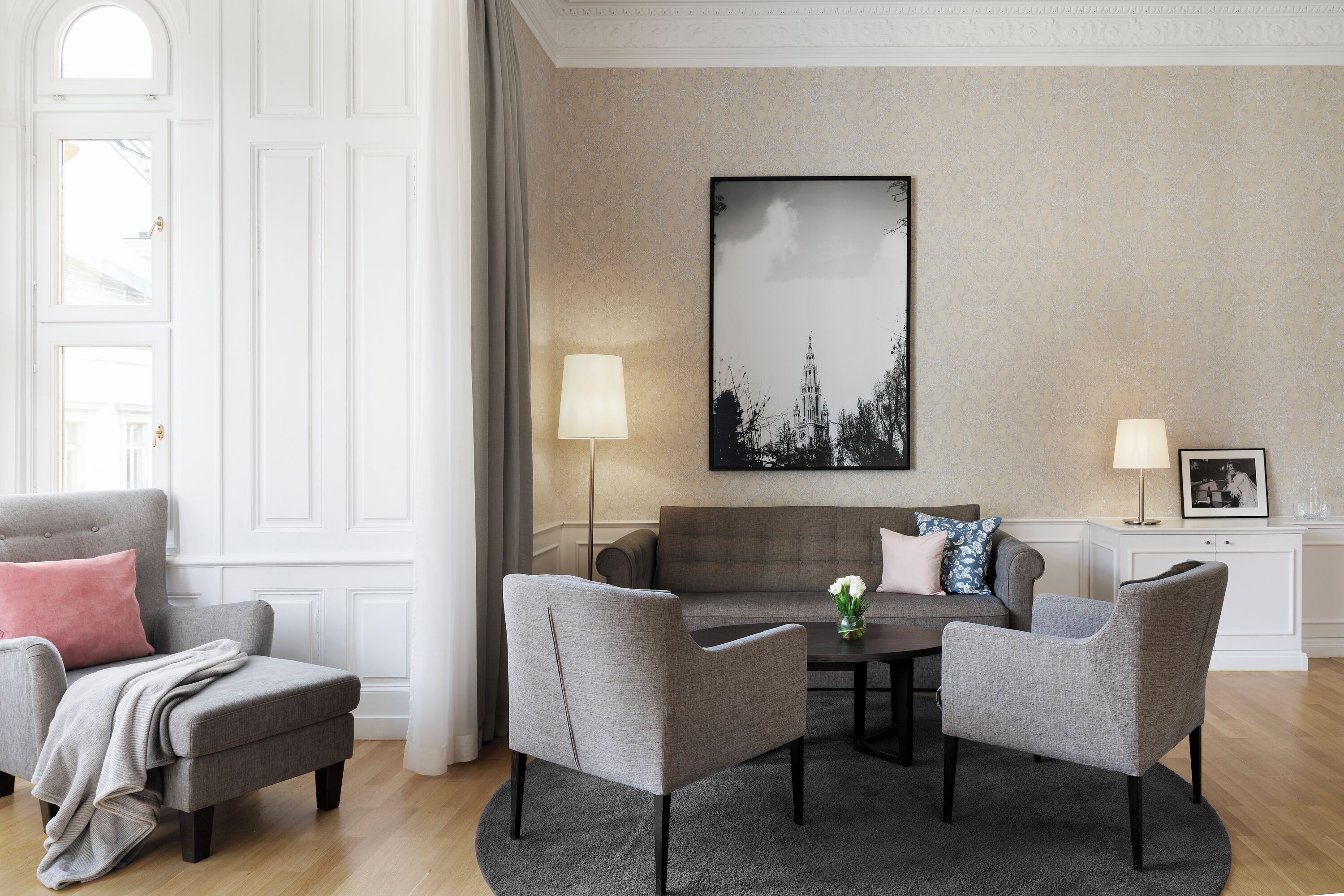 A modern living room with a grey sofa, two armchairs, a coffee table, and a large framed picture on the wall.