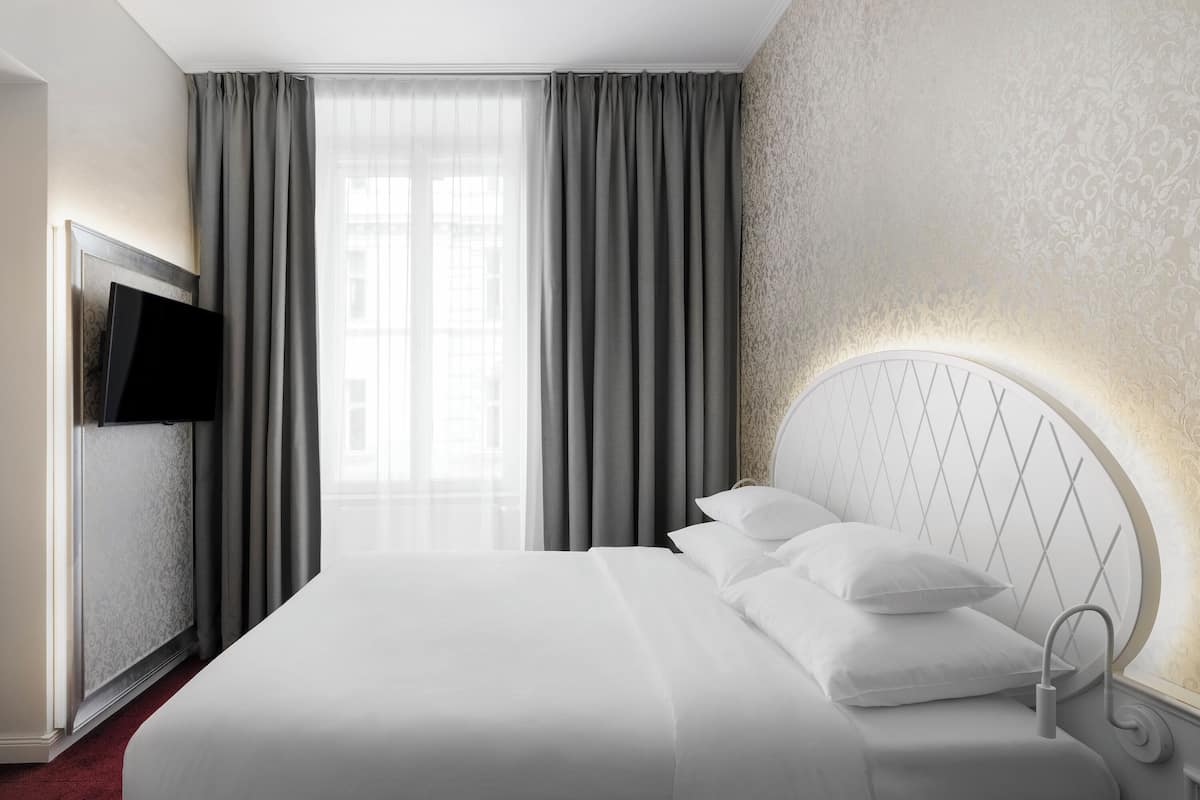 Een hotelkamer met een groot bed, een aan de muur bevestigde televisie en een raam met gordijnen.