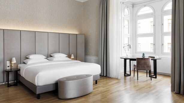 Una habitació d'hotel moderna amb un llit gran, taules de nit, un escriptori i una cadira.