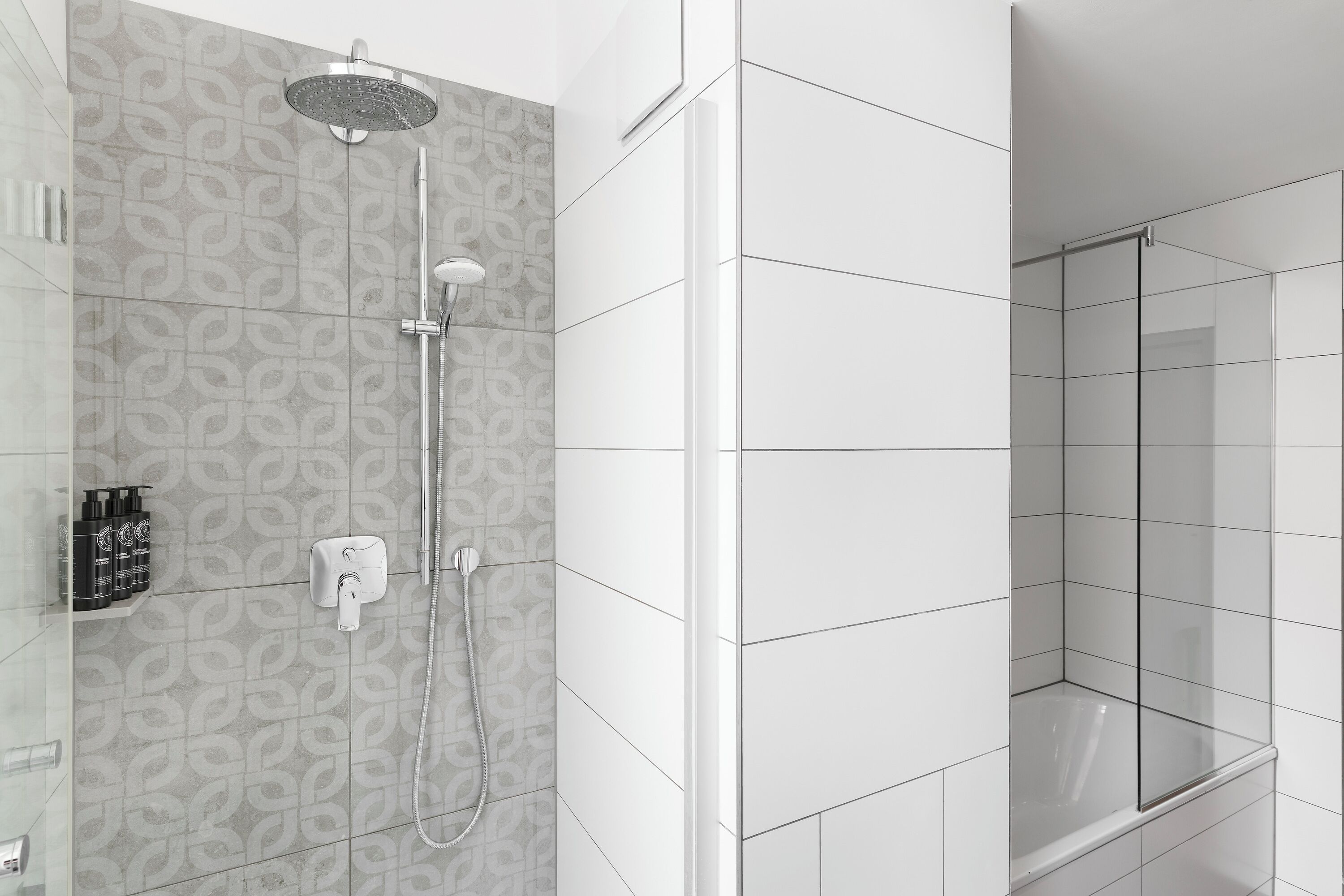 Un baño moderno con ducha, bañera con mampara de vidrio y pared de azulejos con diseño.