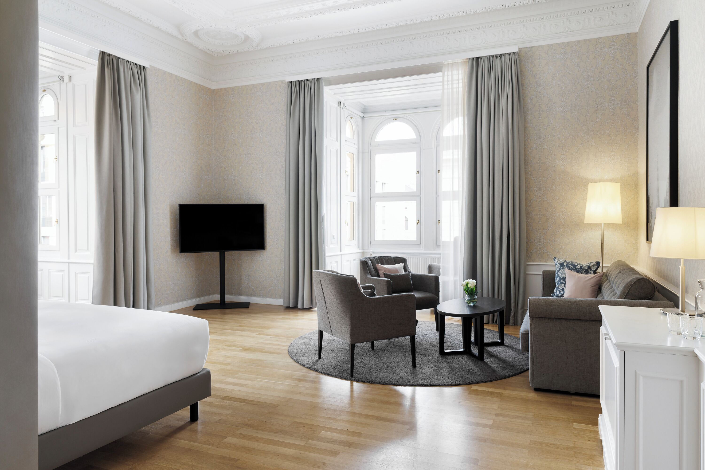 A hotel room with a bed, two armchairs, a sofa, a TV, and a lamp.