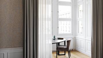 A room with a round table, a chair, and a window with white shutters.