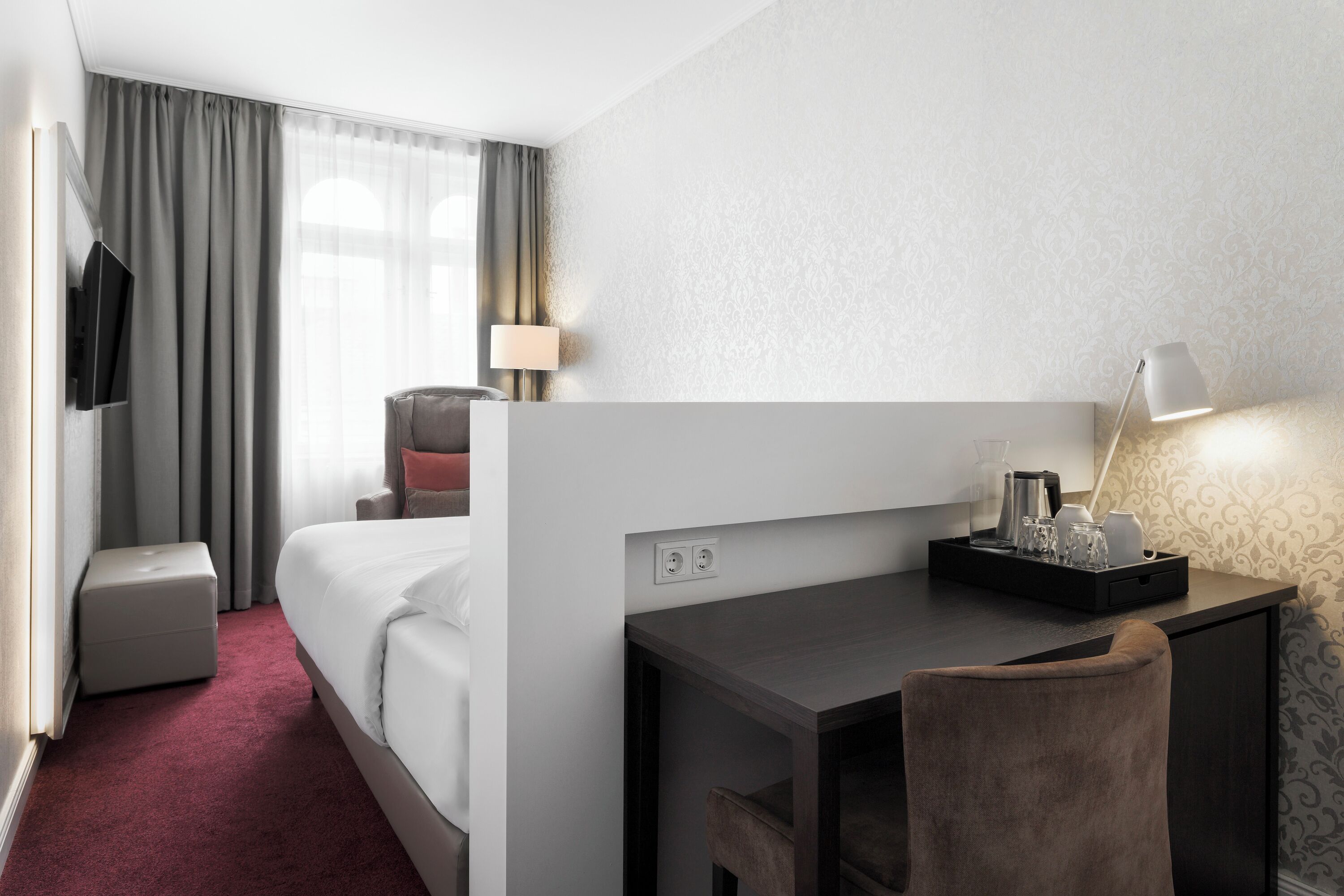 Une chambre d’hôtel équipée d’un lit, d’un bureau, d’une chaise, d’une télévision, d’une lampe et d’un plateau avec divers articles.
