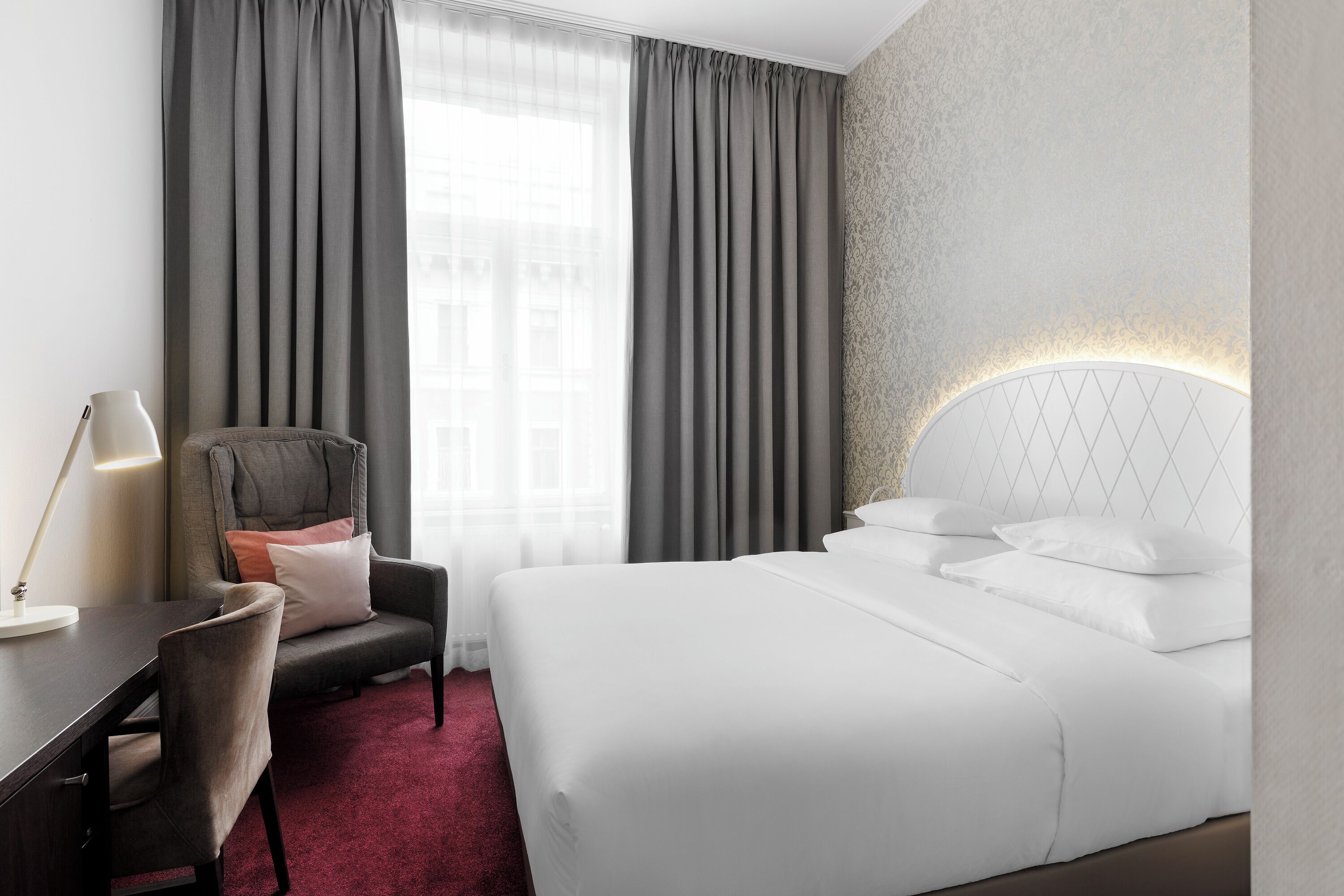 Una habitación de hotel con una cama grande, un escritorio, una silla y un ventanal con cortinas.