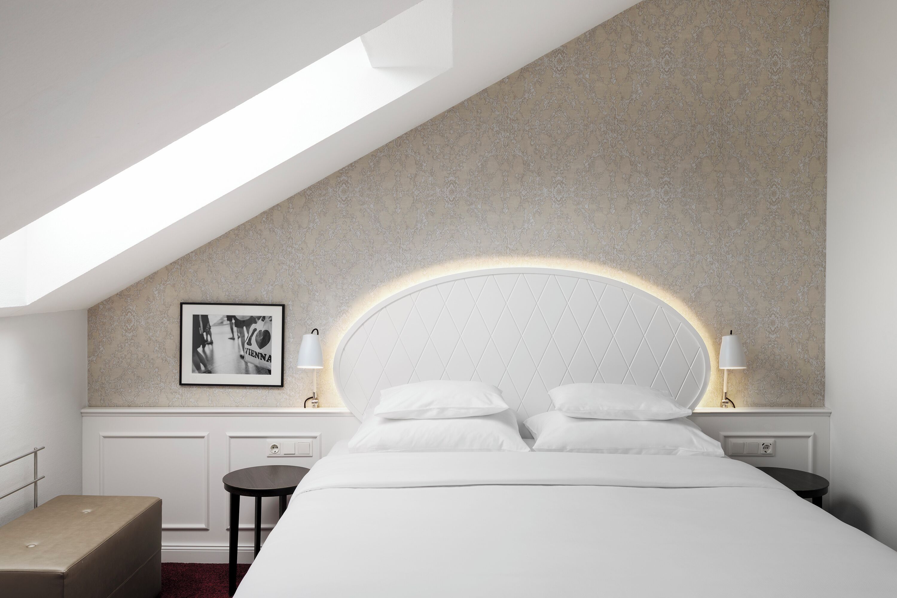 A modern bedroom with a large bed, a round headboard, and a skylight.