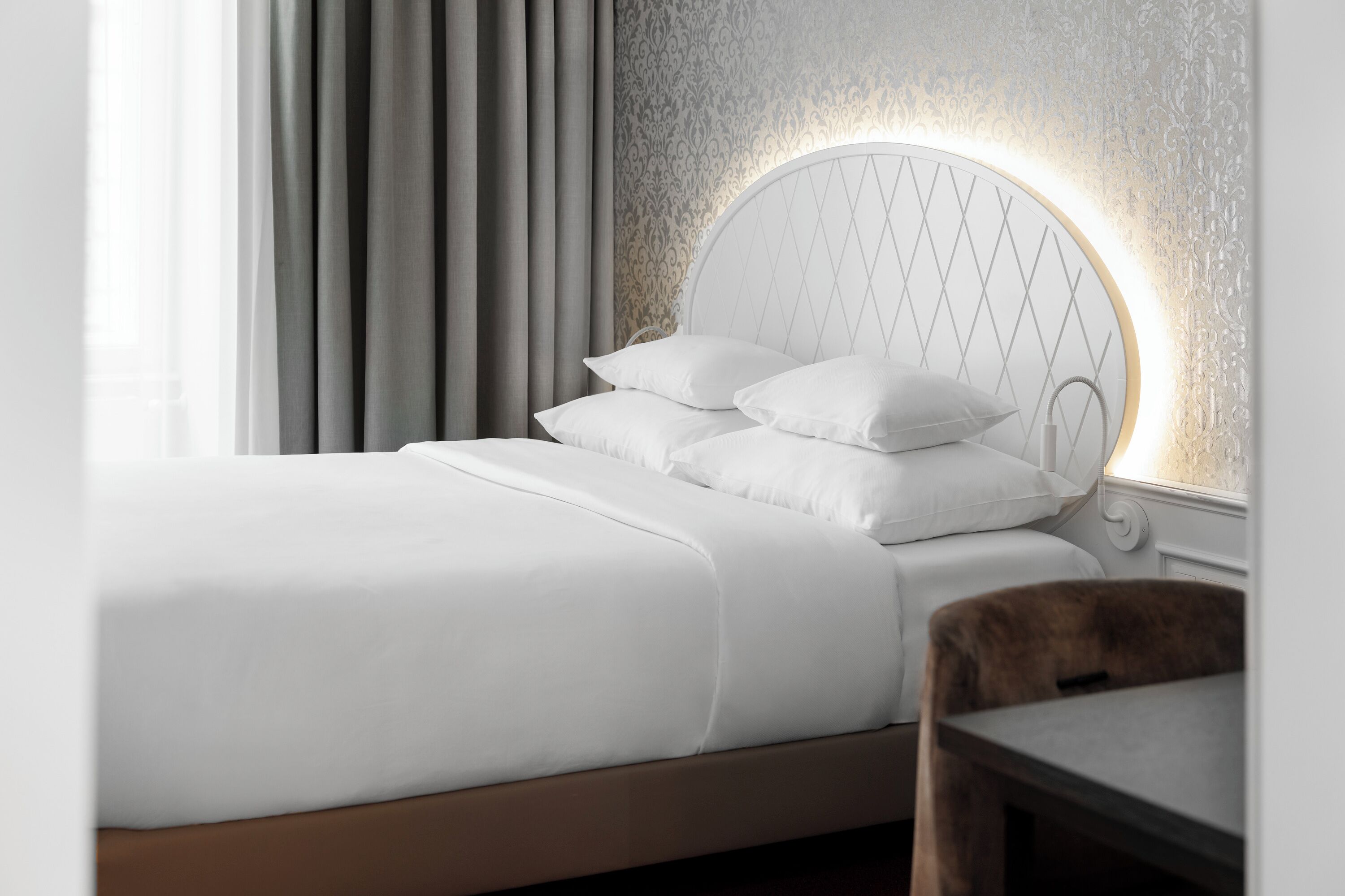 Un lit bien fait, avec du linge de lit blanc et une tête de lit ornée d’un motif géométrique.