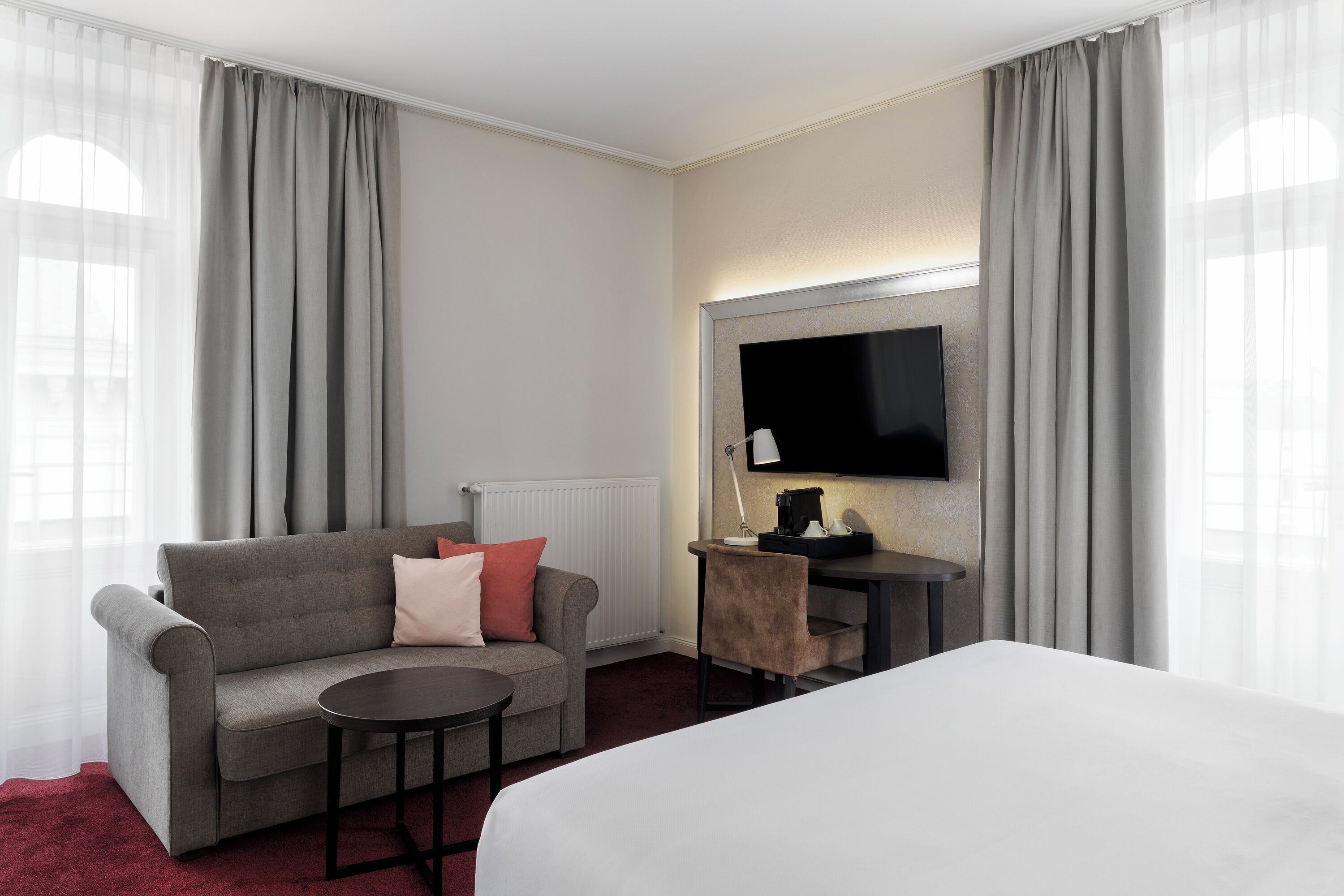 Quarto de hotel com uma cama, um sofá, uma mesa e uma televisão.