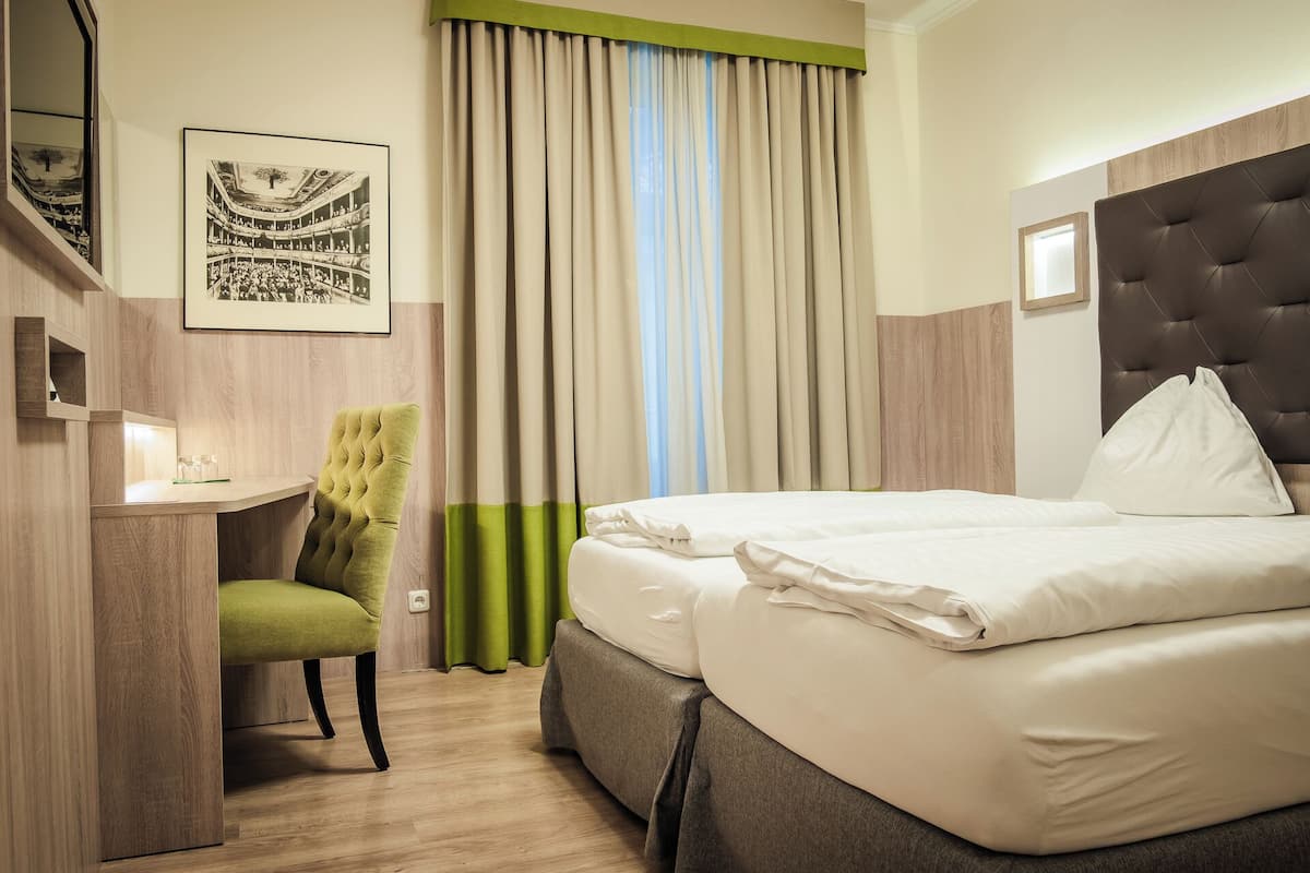 Habitació d'hotel amb un llit, una taula, una cadira, un quadre amb marc i cortines.