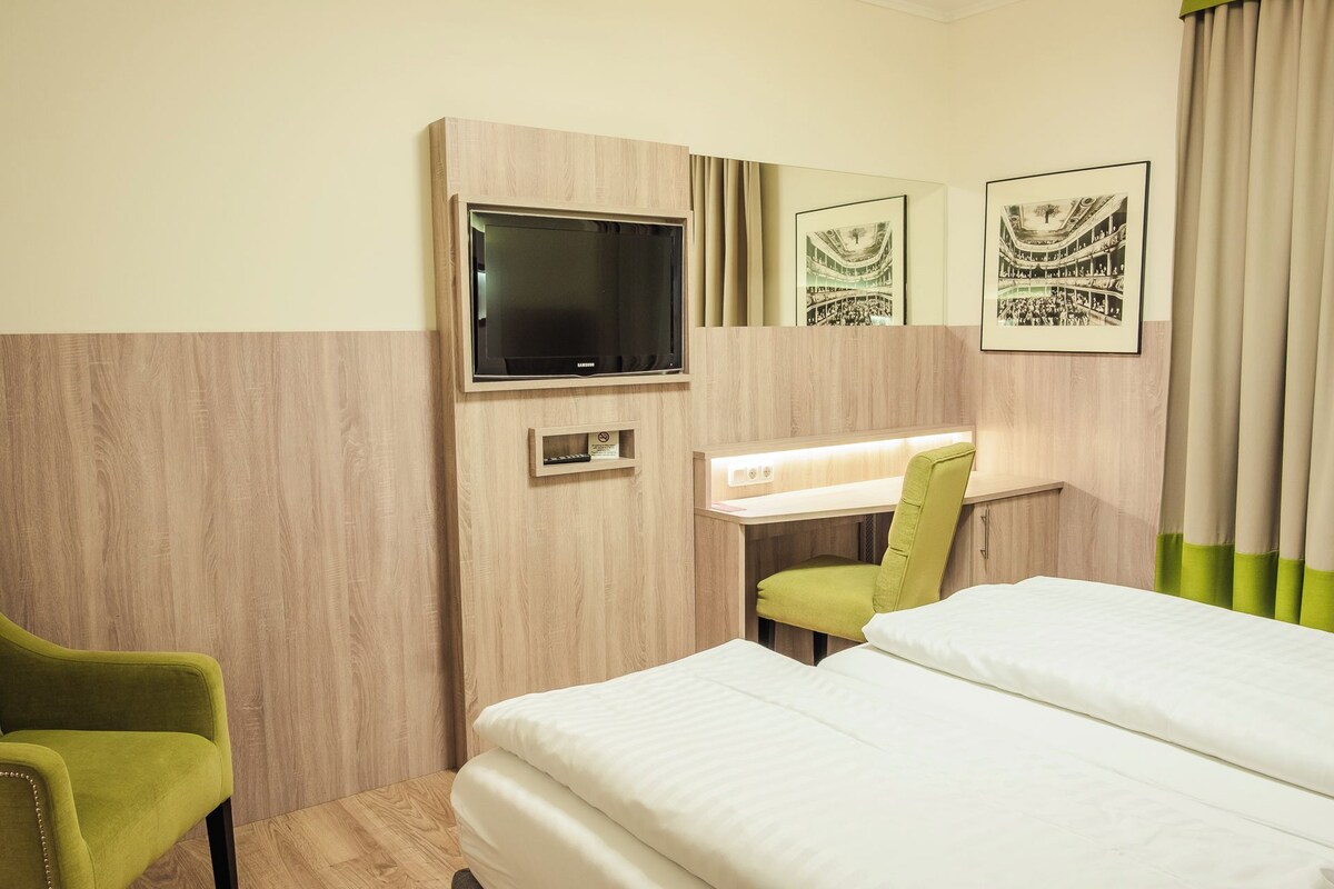 Une chambre d’hôtel avec un lit, un bureau et une chaise, une télévision et des tableaux encadrés au mur.