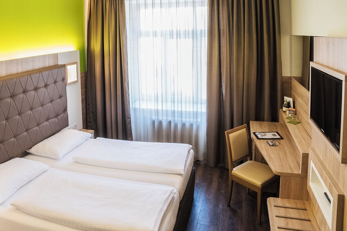 Habitación de hotel con dos camas, un escritorio y una televisión.