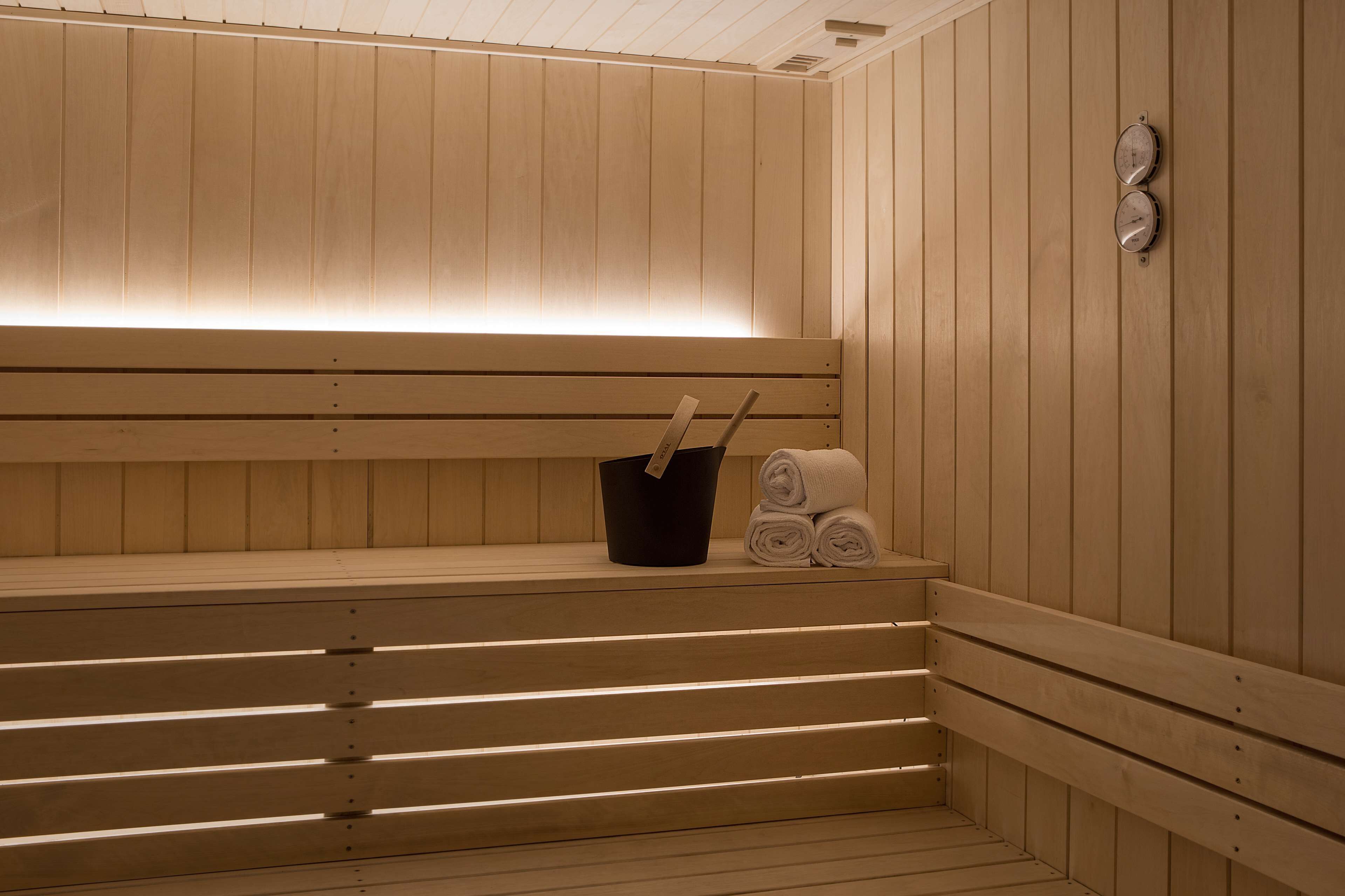 A sauna with wooden benches, a black bucket, and rolled towels.