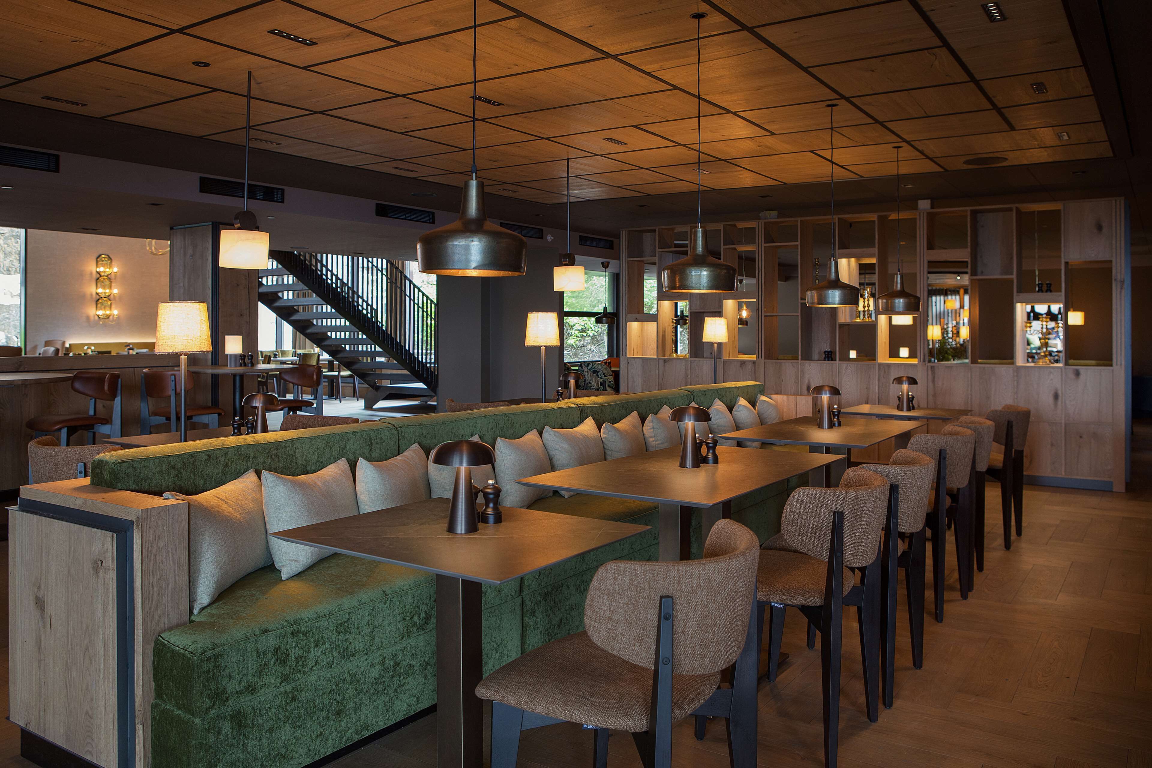 A modern restaurant with a green cushioned bench seating, multiple tables, and pendant lighting.