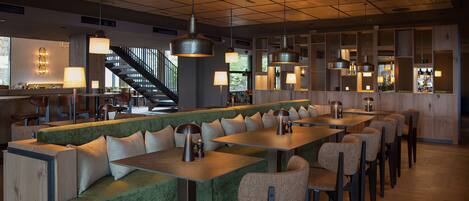 A modern restaurant with a green cushioned bench seating, multiple tables, and pendant lighting.