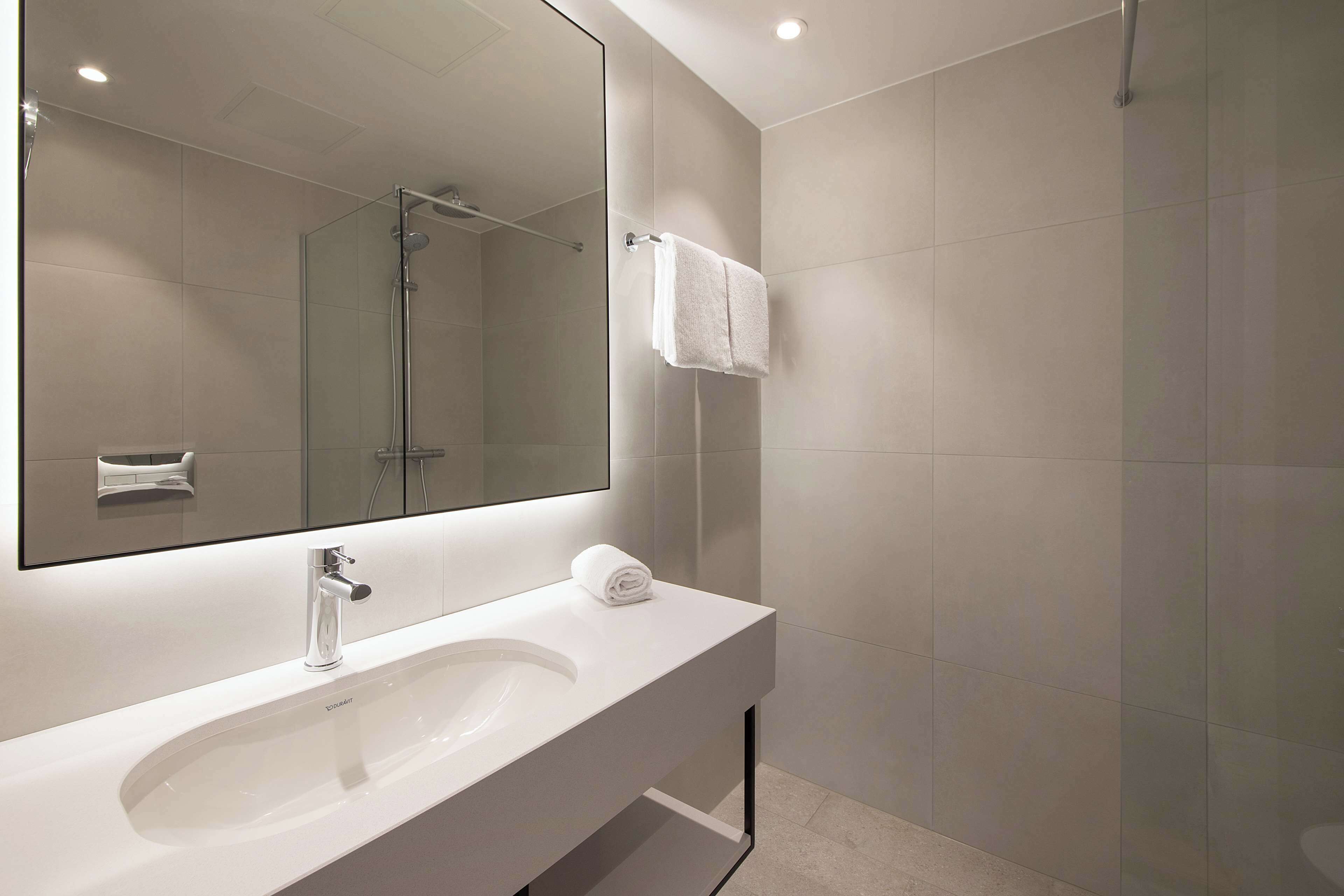 Un baño moderno con un lavamanos blanco, un espejo grande y una ducha con cerramiento de vidrio.