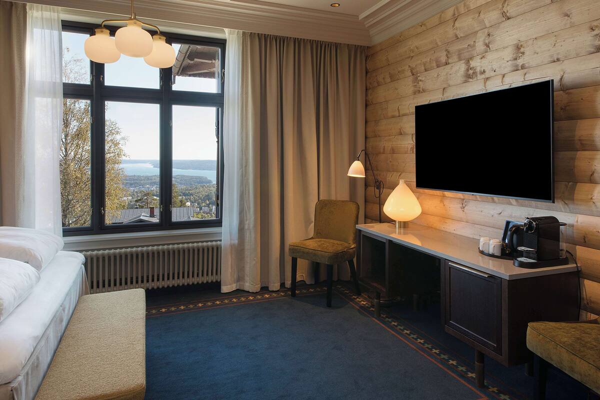 Hotellihuone, jossa on sänky, työpöytä, tuoli, televisio ja ikkuna, josta on näkymä.