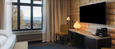 A hotel room with a bed, a desk, a chair, a TV, and a window with a view.