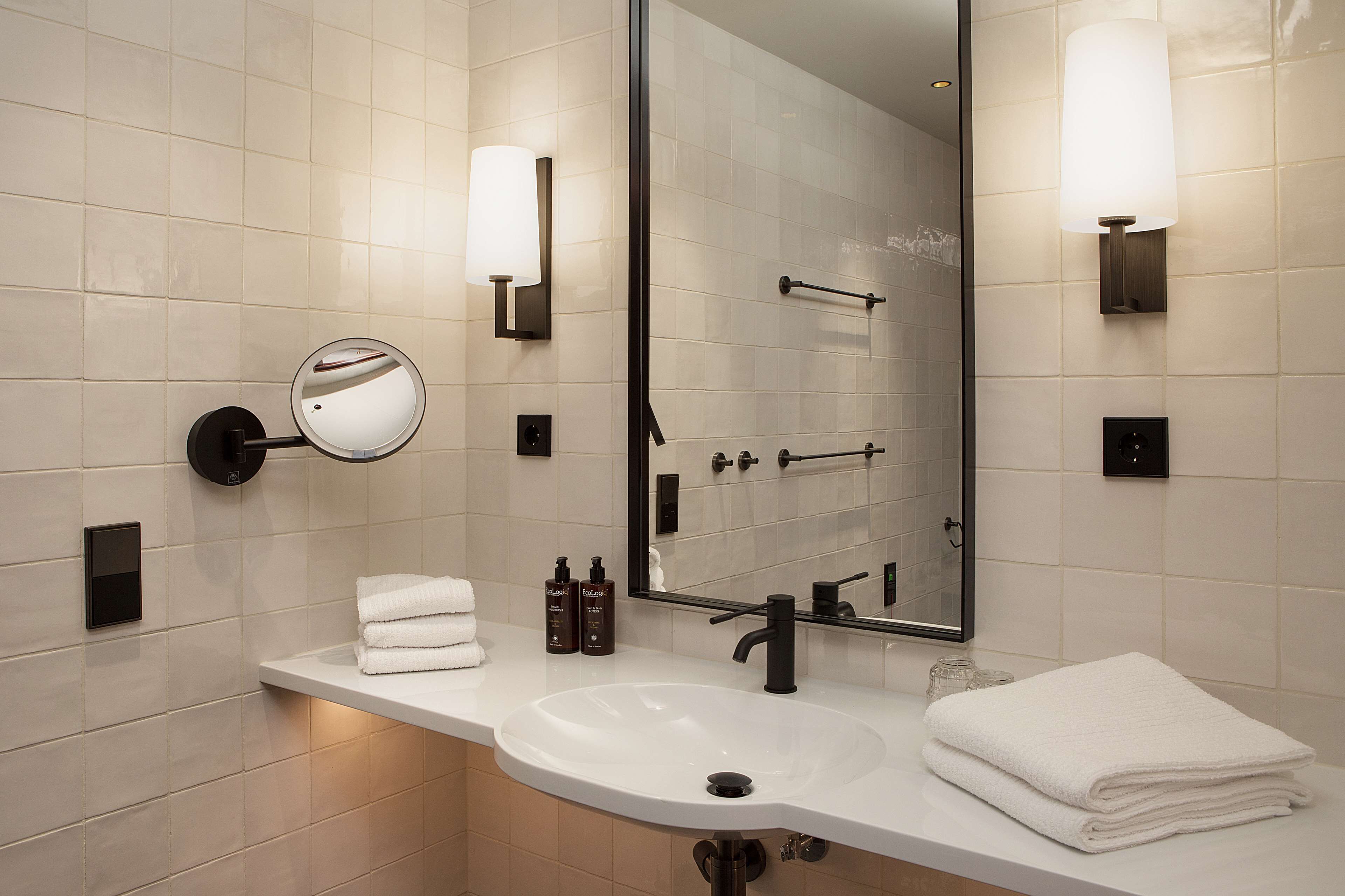 A modern bathroom with a white sink, a large mirror, and two wall-mounted light fixtures.