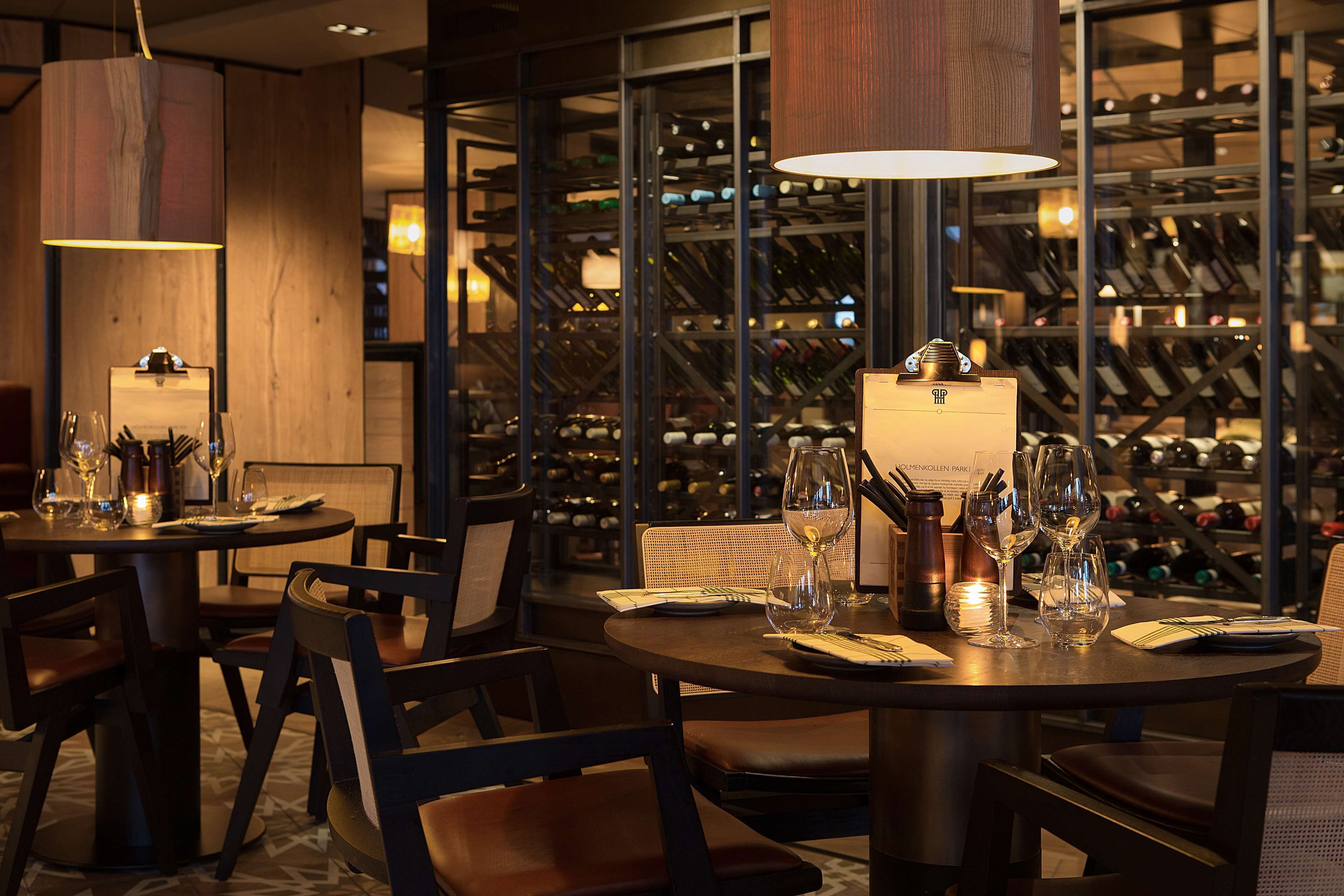 A restaurant with round tables, chairs, and wine glasses. There is a wine rack in the background.