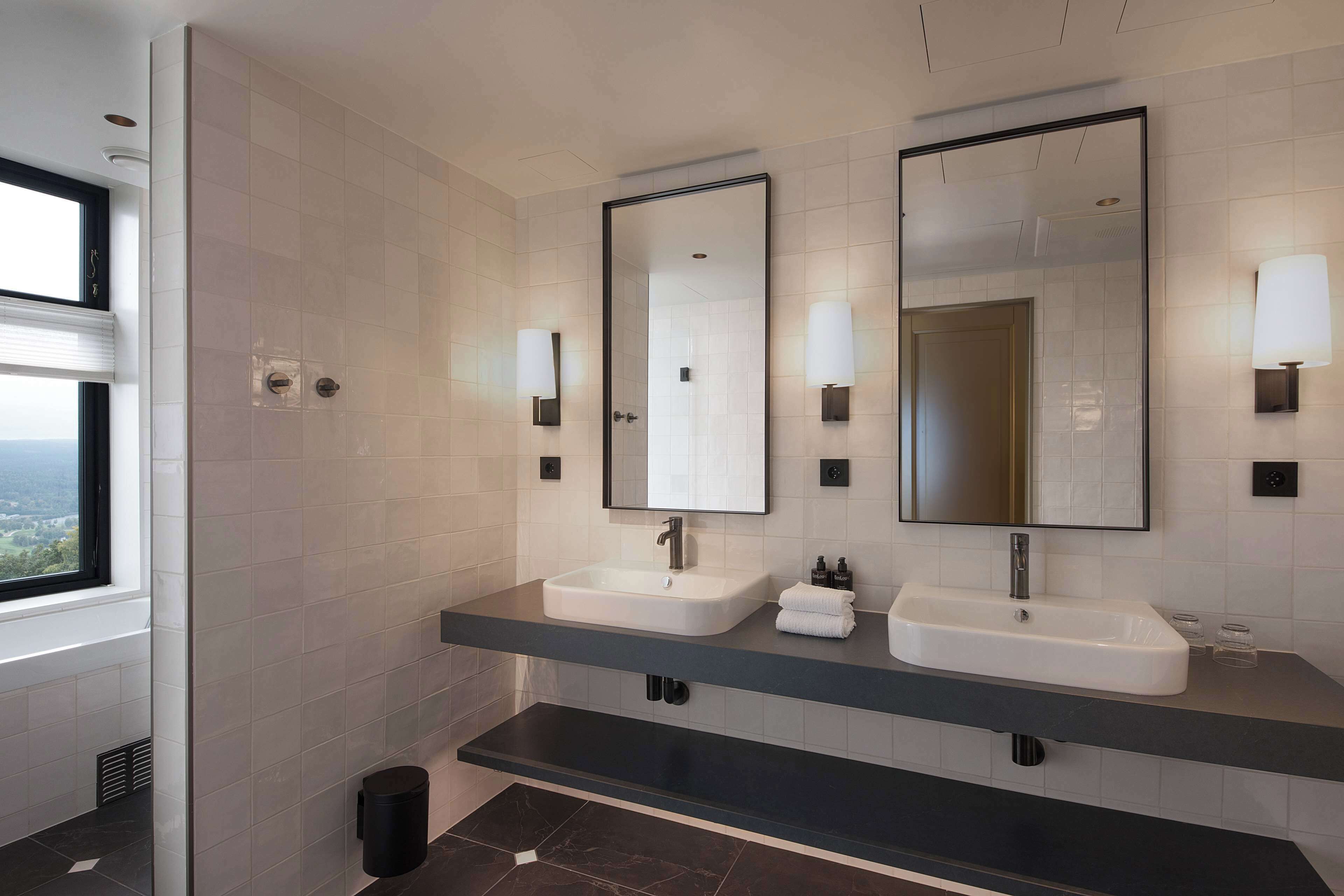 A modern bathroom with two sinks, large mirrors, and wall-mounted lights.