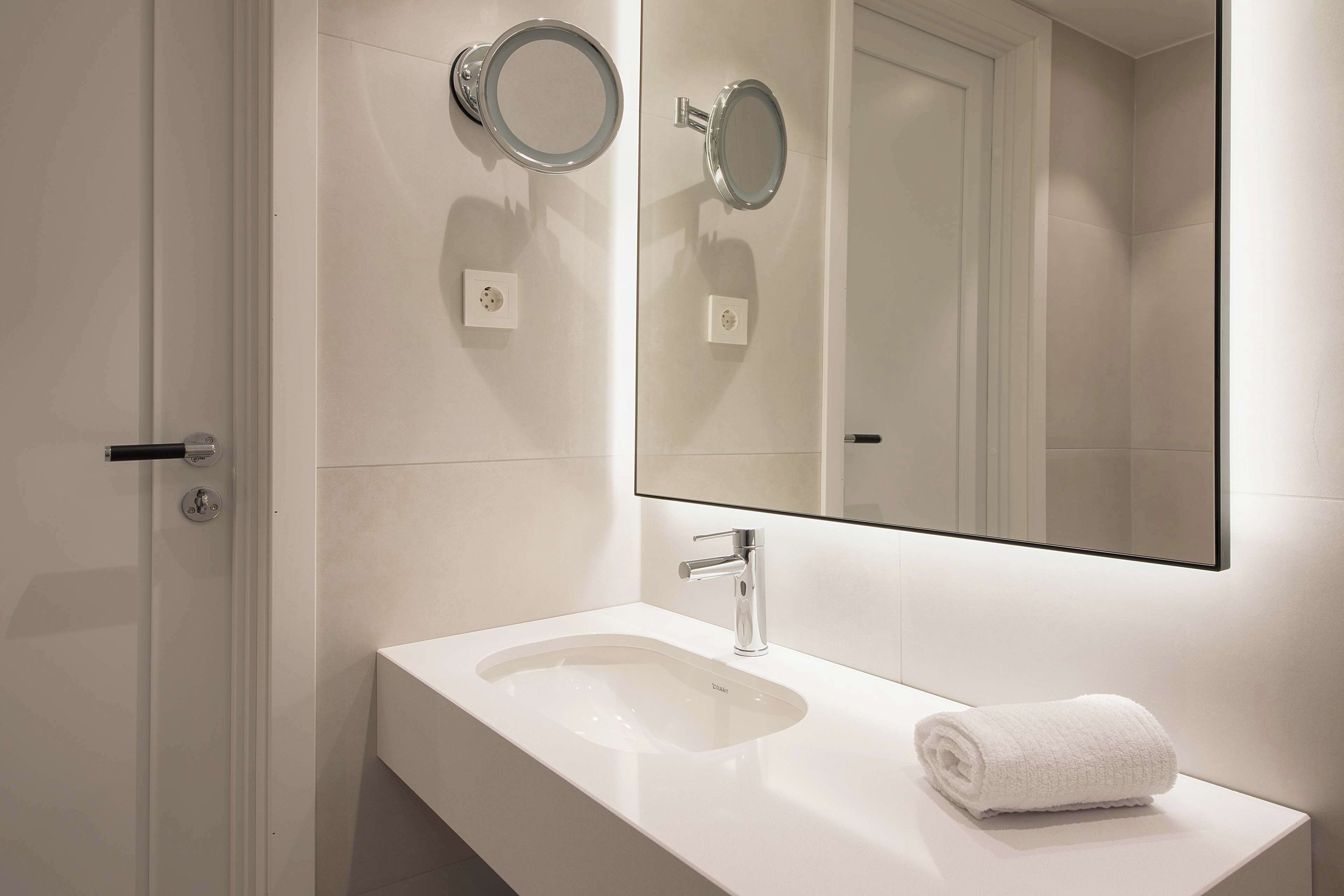 A modern bathroom with a white sink, a large mirror, and a towel on the counter.