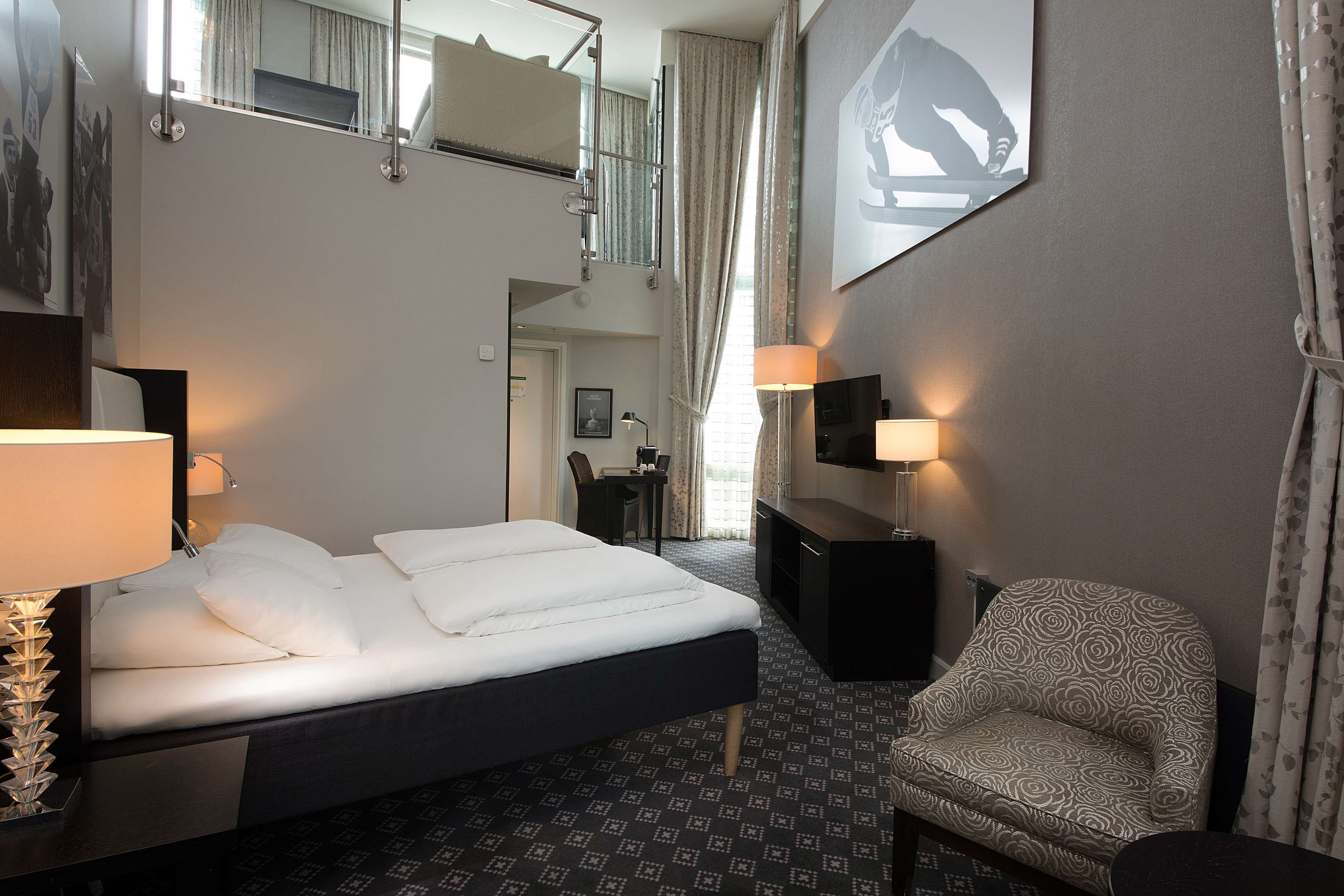 Habitación de hotel con cama, escritorio, silla, televisor y balcón.