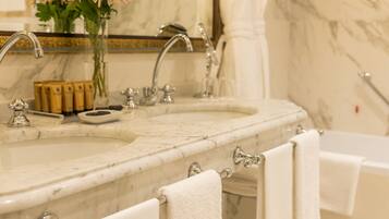 A bathroom with two sinks, a mirror, and a bathtub. There are towels hanging on the side of the bathtub.
