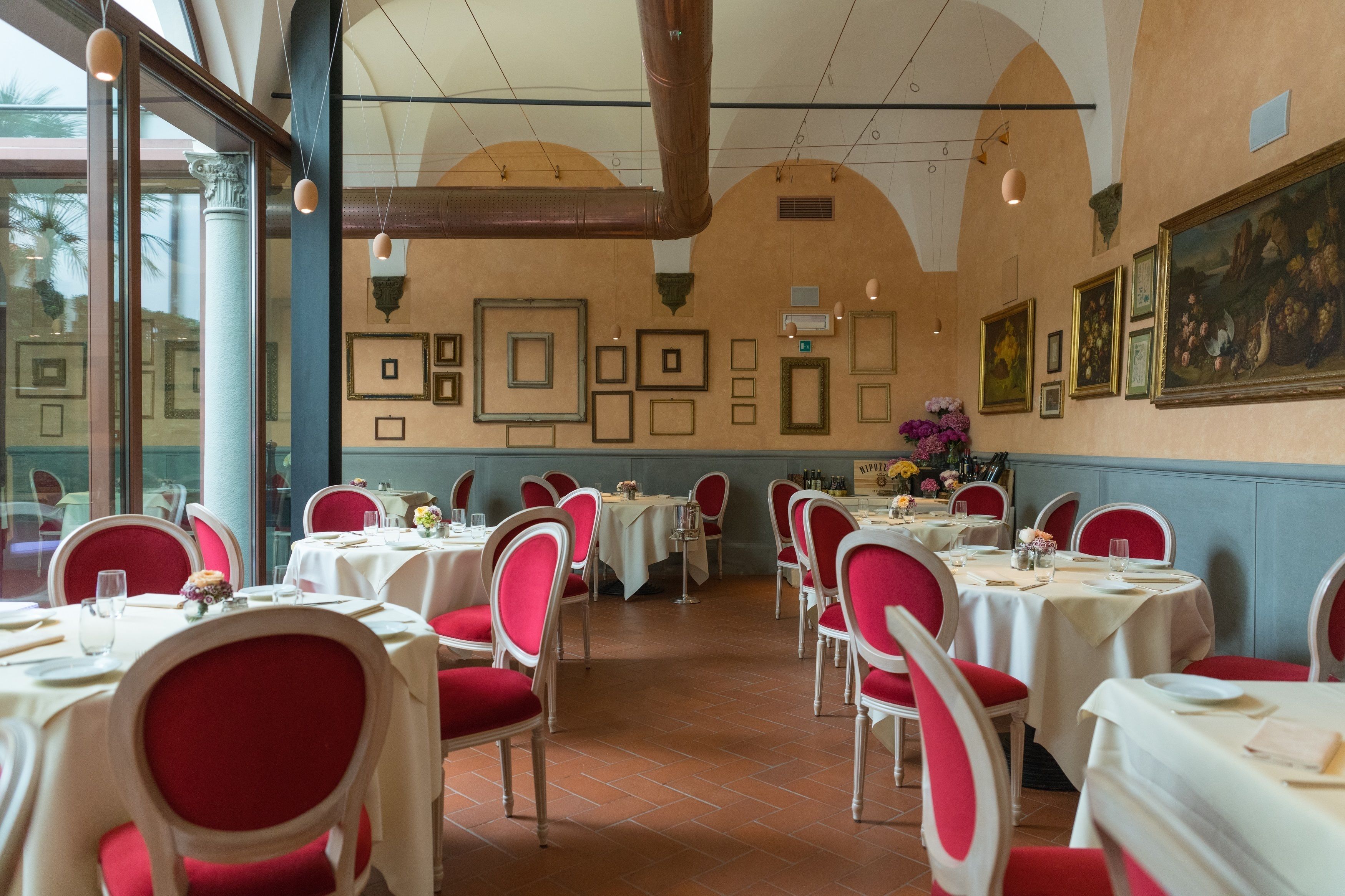 Een restaurant met gedekte tafels, rode stoelen en foto’s in lijsten aan de muur.