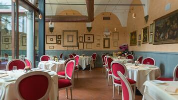 A restaurant with tables set for dining, red chairs, and framed pictures on the walls.