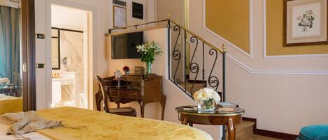 Une chambre d’hôtel avec un lit, un bureau, une chaise, une petite table ornée d’un vase de fleurs et un escalier.